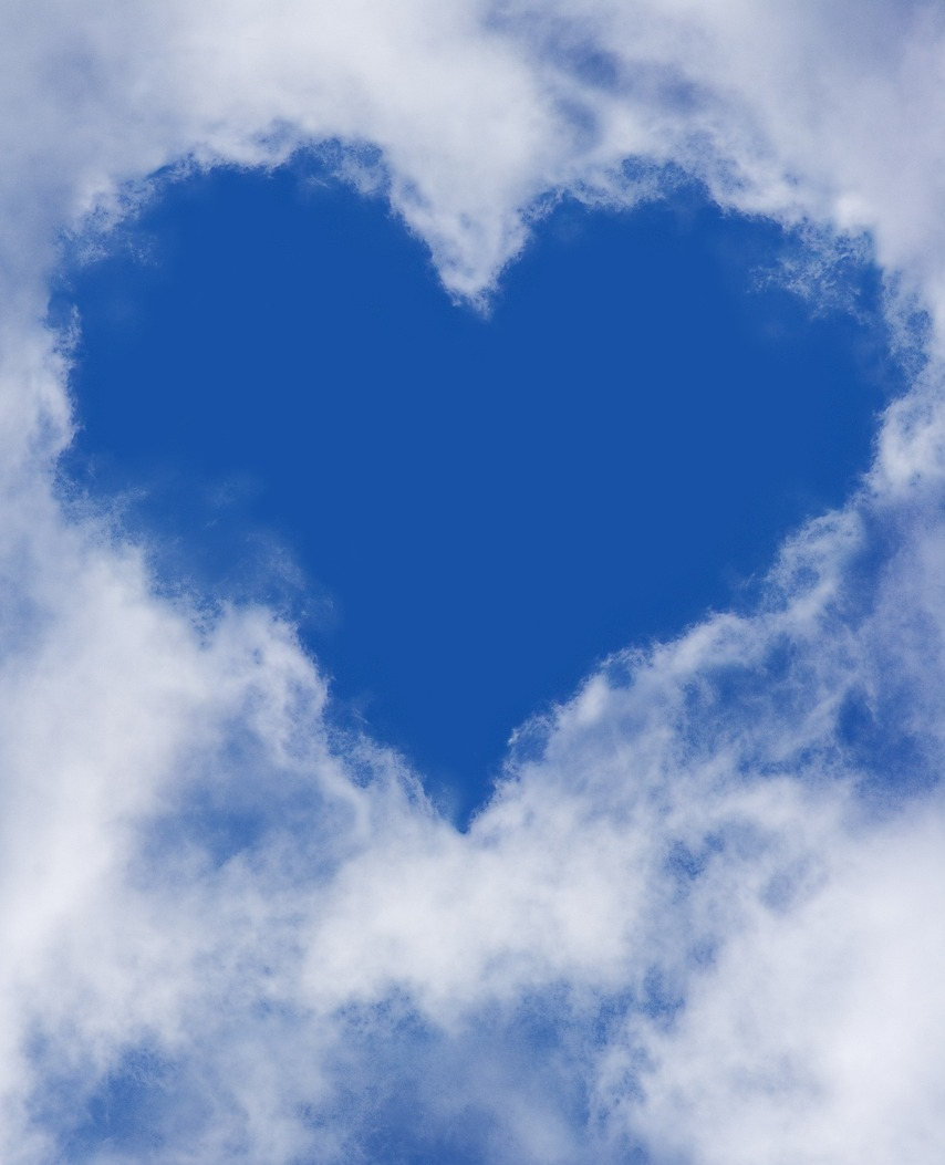 A heart-shaped opening in soft white clouds against a bright blue sky